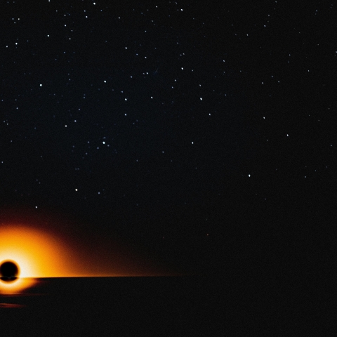 Image showing a black hole in space with mainly black background and the hole showing with a glowing ring of yellow, orange and red colour tones