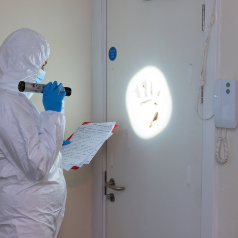 A student in forensic protective gear shining a light on a handprint on a door