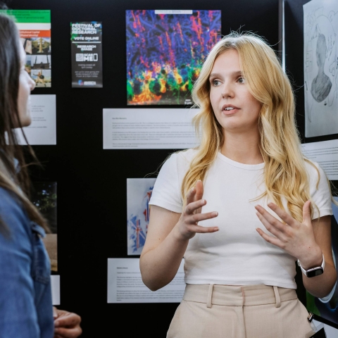 Postgraduate student standing by a poster board explaining the poster 