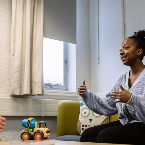 Woman talking to another person, next to a table with a toy on it.