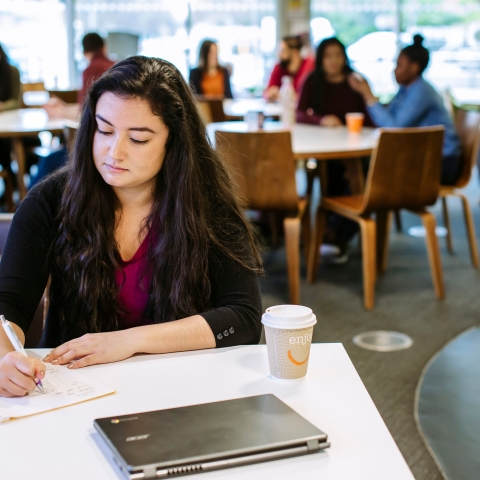 Student taking notes in university library cafe