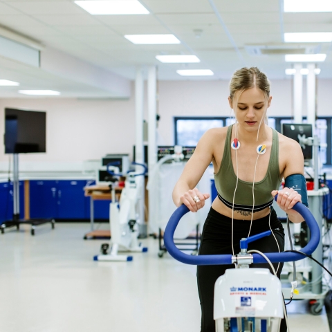 Student on bike machine with a trainer and hooked up to monitors