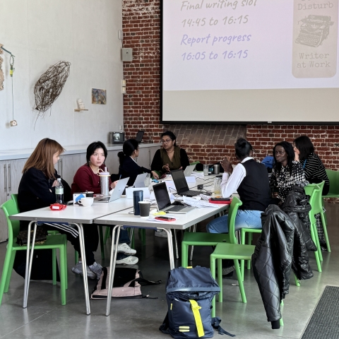 Eight postgraduate research students sat around a large rectangle table with laptops at the writing retreat