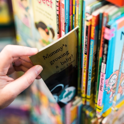 Teacher's hand extracting early years book from shelf