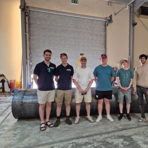 Students next to a mock-up of the rocket in the factory