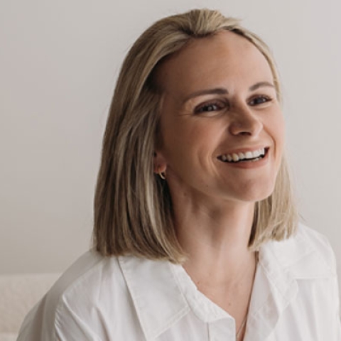 Graduate, Natty, has blonde hair and is wearing a white shirt on a photoshoot - in the photo, she is smiling off camera