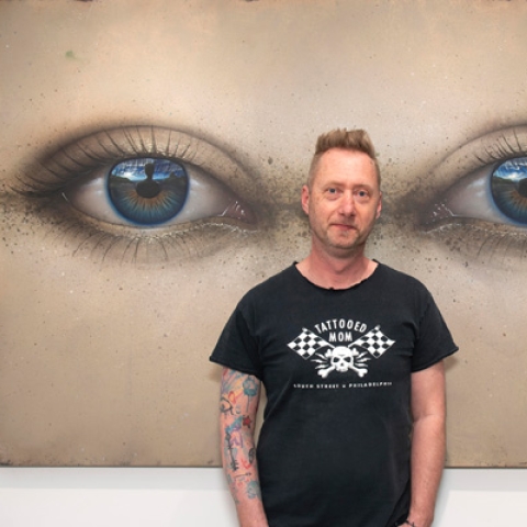 Paul Stone standing in front of his artwork smiling to camera wearing black tshirt