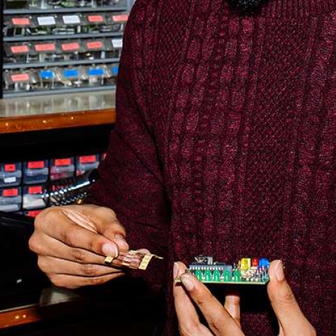 Male student in jumper working on a circuit board with a row of electrical components behind him
