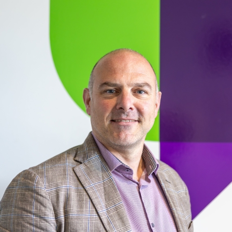 Portrait of Professor Richard Thelwell standing in front of University of Portsmouth logo