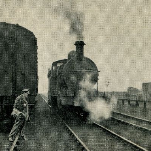 Black and white picture of a man crossing train tracks in front of two trains.