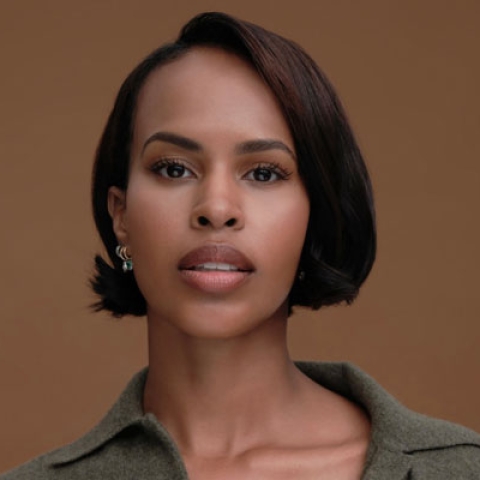 Headshot of Sabrina Dhowre Elba looking to camera wearing green shirt against backdrop