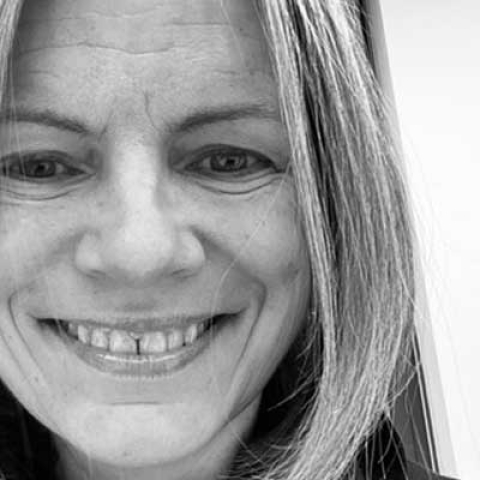 A black and white picture of alumna, Sarah Caddick smiling to camera