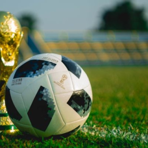 The world cup trophy next to a football on a football pitch