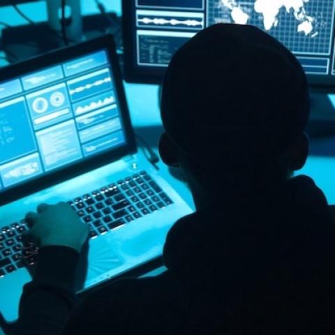 a hacker in the dark looking at computer screens