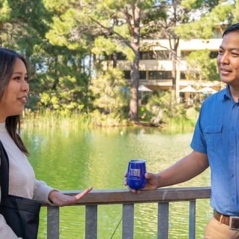 three people talking on a bridge in front of a lake