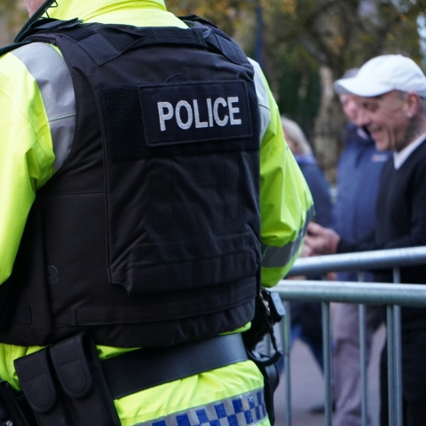 Image of the back of a policeman in a crowd wearing fluorescent jacket and bullet proof vest