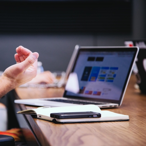 A laptop on a table and a person's hands gesticulating