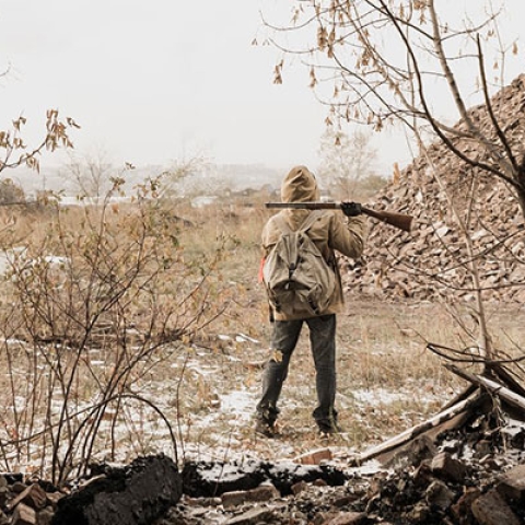 A lone soldier with a gun stands in a desolate landscape