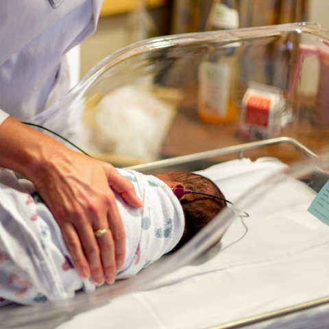 Person in white scrubs holding hand over baby in hospital