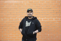 International student Aziz wearing a black baseball cap against a brick wall