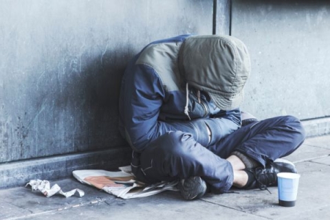 Homeless person sitting on sidewalk with head down