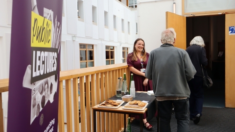 Two people entering the lecture theatre being greeted by a member of staff