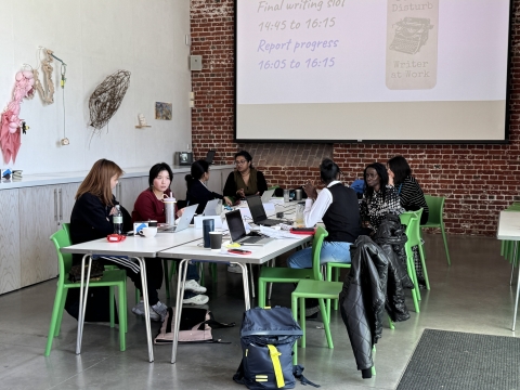Eight postgraduate research students sat around a large rectangle table with laptops at the writing retreat