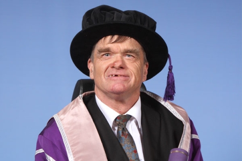 Kevin Holmes holding scroll in graduation gown and cap smiling to camera