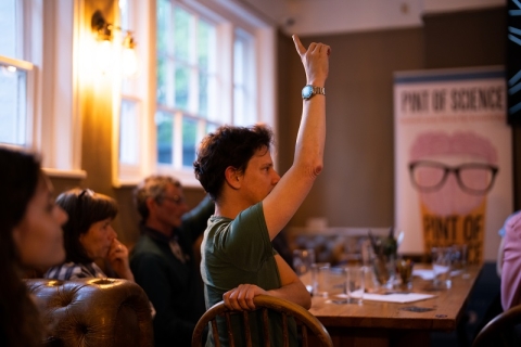 A man raising his hand in a pub with a Pint of Science sign in the background