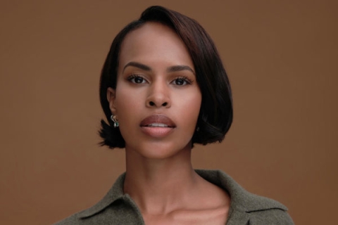 Headshot of Sabrina Dhowre Elba looking to camera wearing green shirt against backdrop