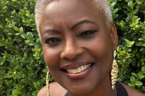 Image of Samantha Tross smiling to camera wearing gold dangly earrings against greenery backdrop
