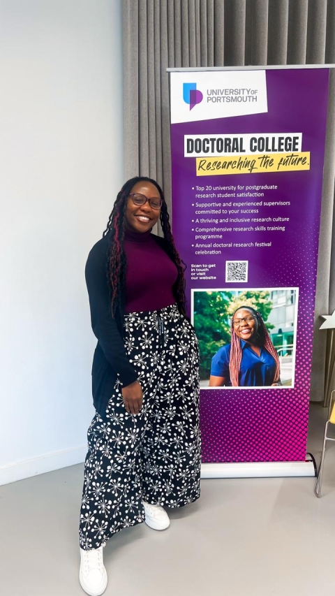 International Student Ritah smiling next to a promotional banner with her photo on