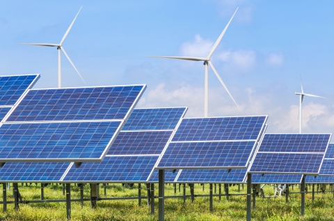 Rows of solar panels, with wind turbines in the background