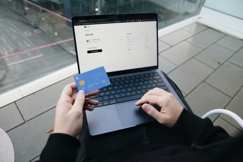 Image shows someone using a laptop and holding a debit or credit card as if purchasing an online product or service