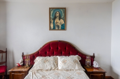 a picture of a rustic bed with a painting of jesus hanging over it by Nicola De Sa