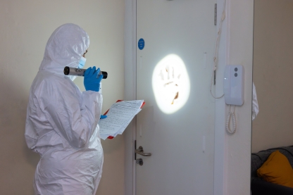 A student in forensic protective gear shining a light on a handprint on a door
