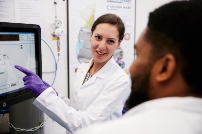 Two students in lab coats consulting at a screen