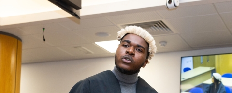 A man standing in a replica law court wearing a solicitors robe a white periwig