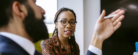 Two business professionals in a meeting, with a woman listening to a colleague speaks.