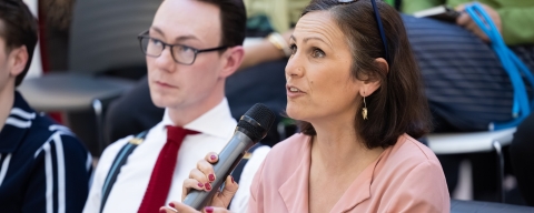 A woman in a pink blouse speaking through a microphone