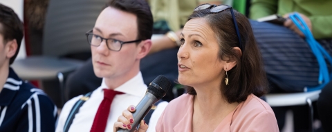 A woman in a pink blouse speaking through a microphone