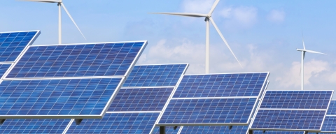 Rows of solar panels, with wind turbines in the background