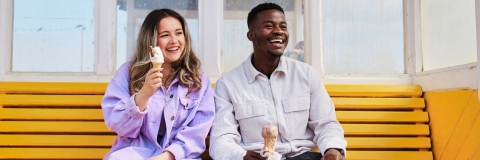 Two students seated on a bench, happily eating ice cream together