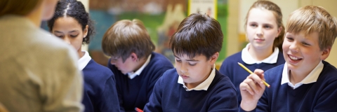 School children in a classroom, sitting at a desk with workbooks
