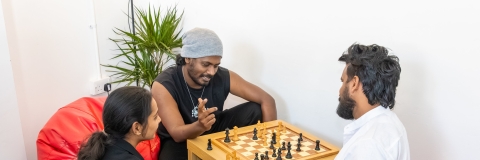 Three students sitting around a chess board 