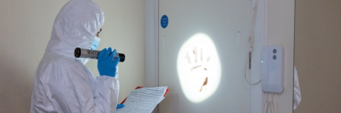 A student in forensic protective gear shining a light on a handprint on a door