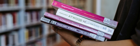 Student holding a pile of books at a library