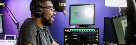 Alumnus Nels Hylton behind a microphone in the studio at BBC Radio One