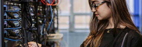 Student adjusts ethernet cables on server wall in Technology Facilities