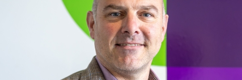 Portrait of Professor Richard Thelwell standing in front of University of Portsmouth logo